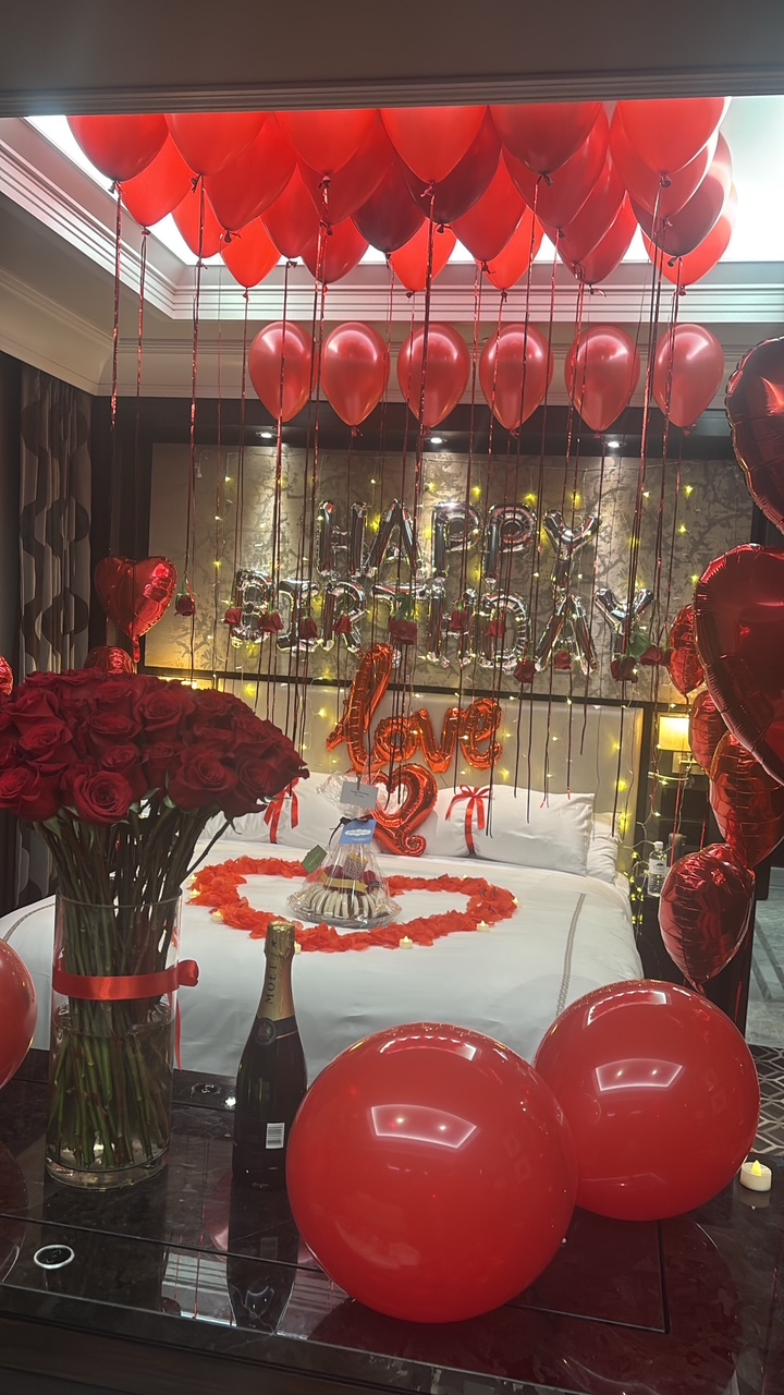Suite styled with red balloons, roses, champagne and a rose petal heart on the bed
