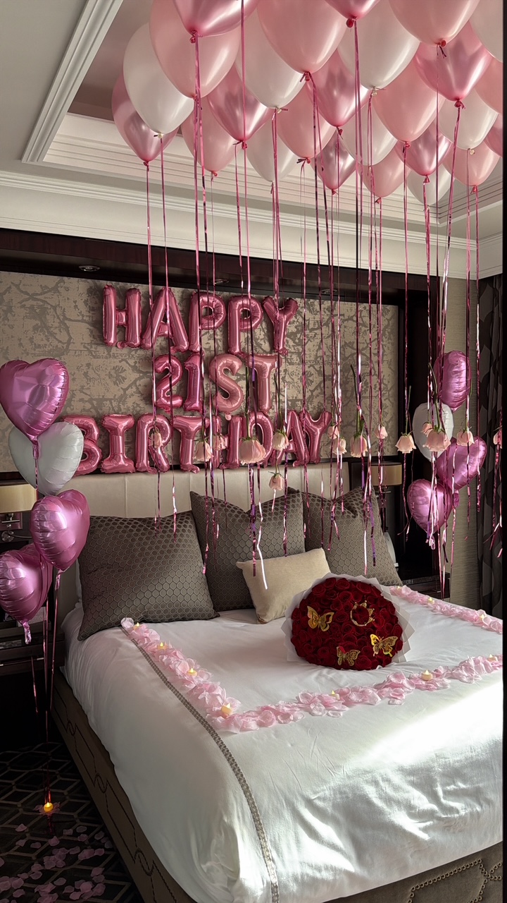Suite styled with pink ceiling balloons, a Happy 21st Birthday foil banner, hearts and a rose bouquet on the bed